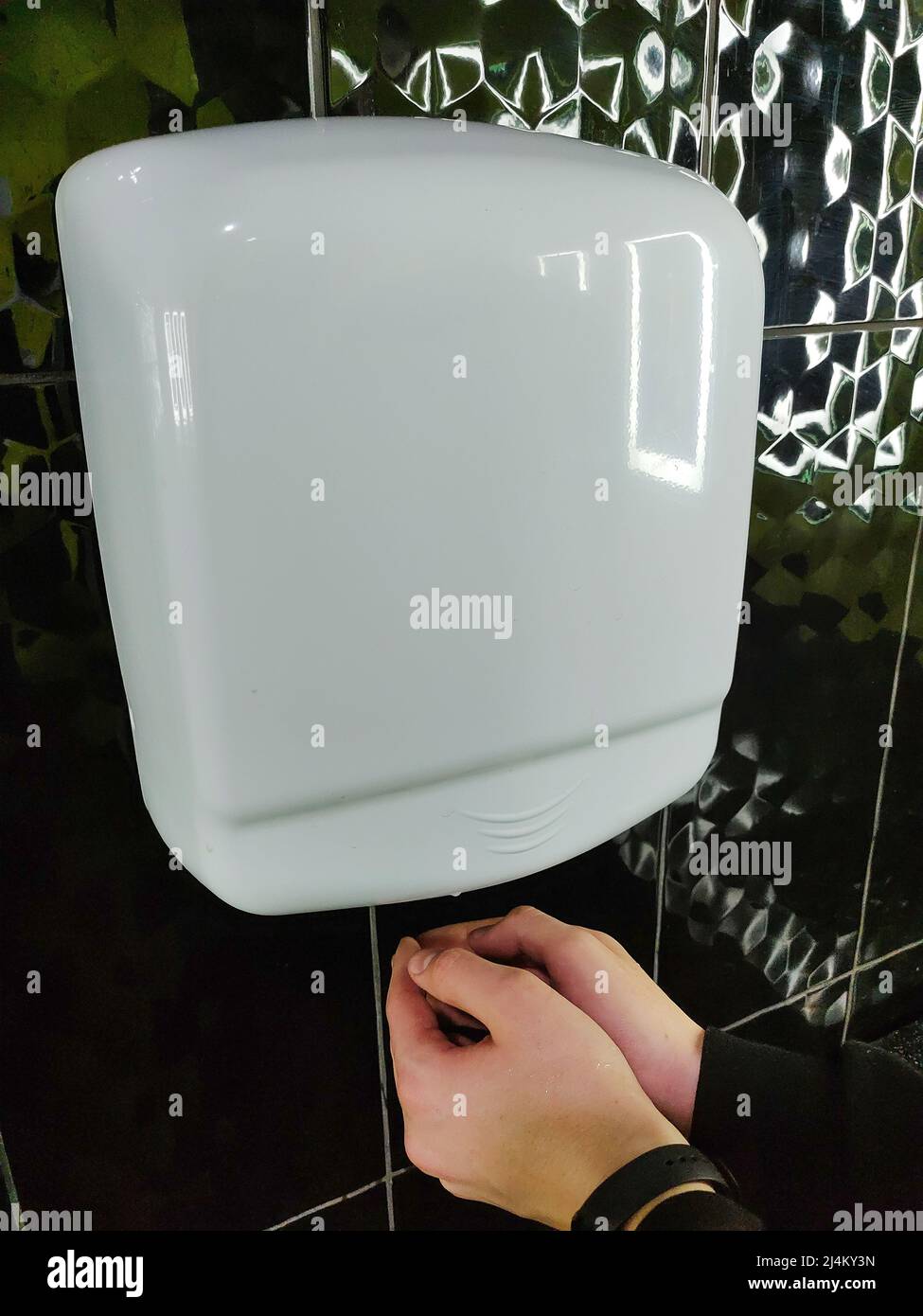 Le sèche-mains automatique à air est suspendu au mur et les mains des enfants sont séchées sous le mur Banque D'Images