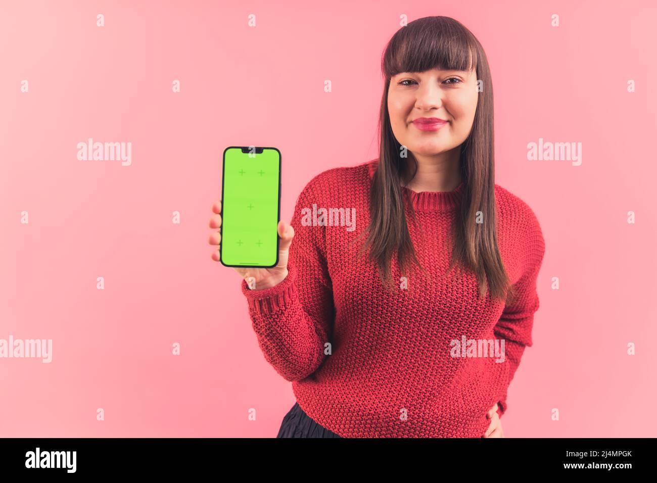 Belle femme caucasienne tient le téléphone maquette avec écran vert regardant l'appareil photo. Espace de copie isolé sur fond rose. Photo de haute qualité Banque D'Images