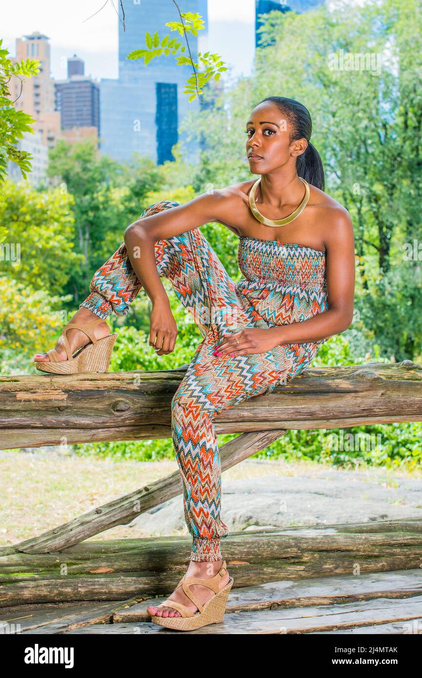 Vêtue d'un haut et d'un pantalon sans bretelles tendance et de style  contemporain, cette jolie femme noire est assise sur de petits bois dans  une grande ville, relaxée Photo Stock - Alamy