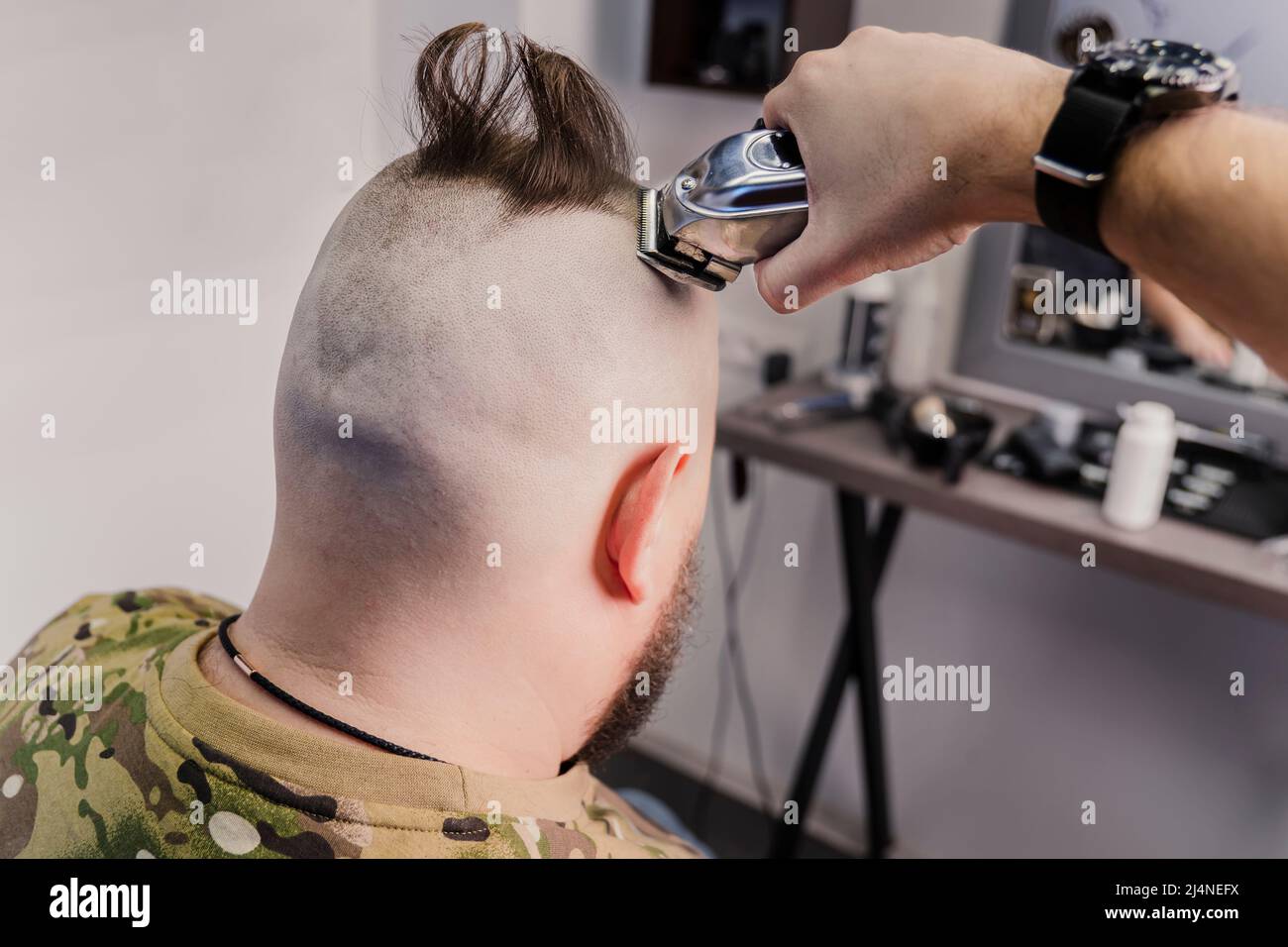 Un jeune homme dans un uniforme militaire se prépare à la tête chauve pour le service militaire. Un homme avec une barbe obtient une coupe de cheveux dans un salon de coiffure. Banque D'Images