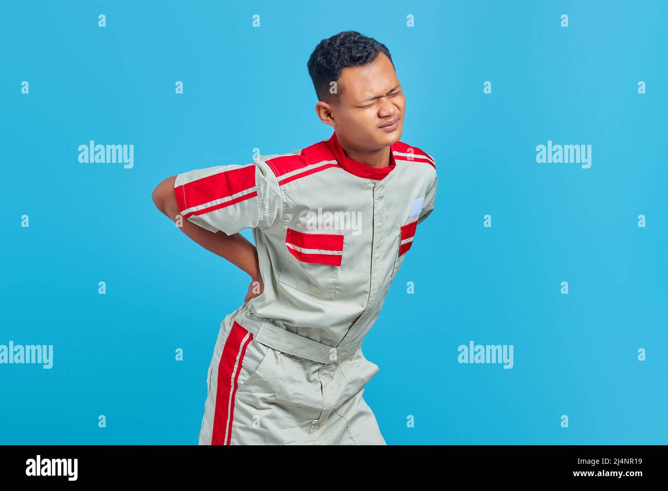 Portrait d'un jeune mécanicien asiatique souffrant de douleurs dorsales et touchant les mains sur fond bleu Banque D'Images