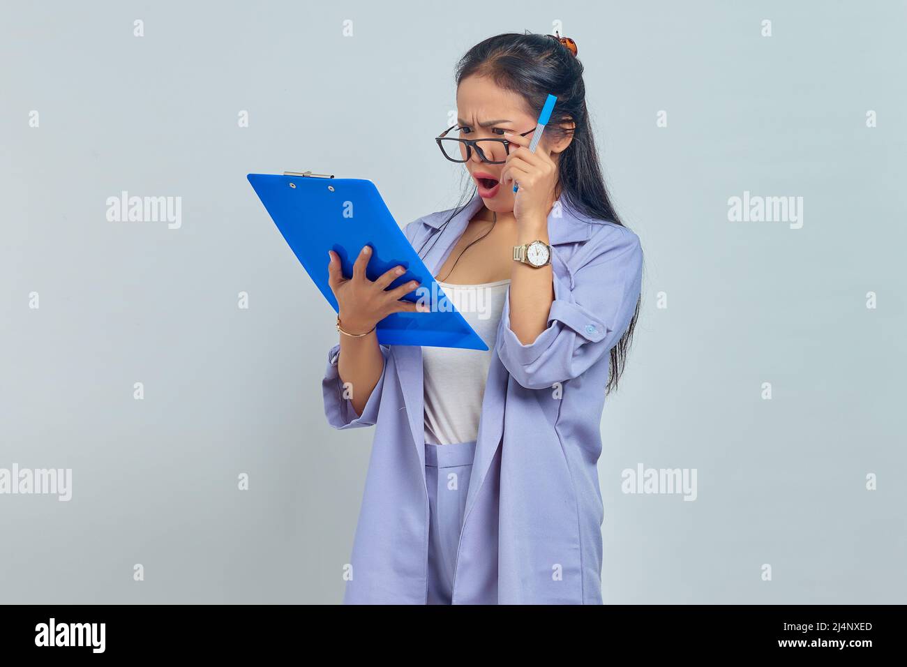 Portrait d'une jeune femme d'affaires asiatique surprise regardant la liste d'emploi sur presse-papiers isolé sur fond violet Banque D'Images