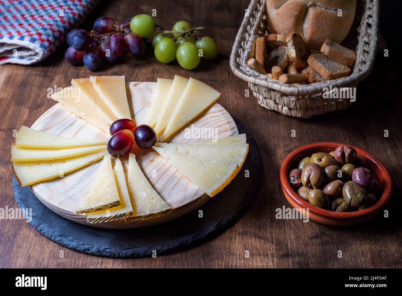 Plateau de fromages espagnols accompagné de raisins, d'olives et de pains variés. Sur fond en bois. Banque D'Images