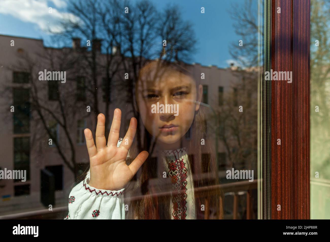 Une fille avec un visage triste dans une robe brodée se tient près de la fenêtre. La jeune fille proteste contre la guerre et montre du patriotisme et de l'amour pour l'Ukraine Banque D'Images