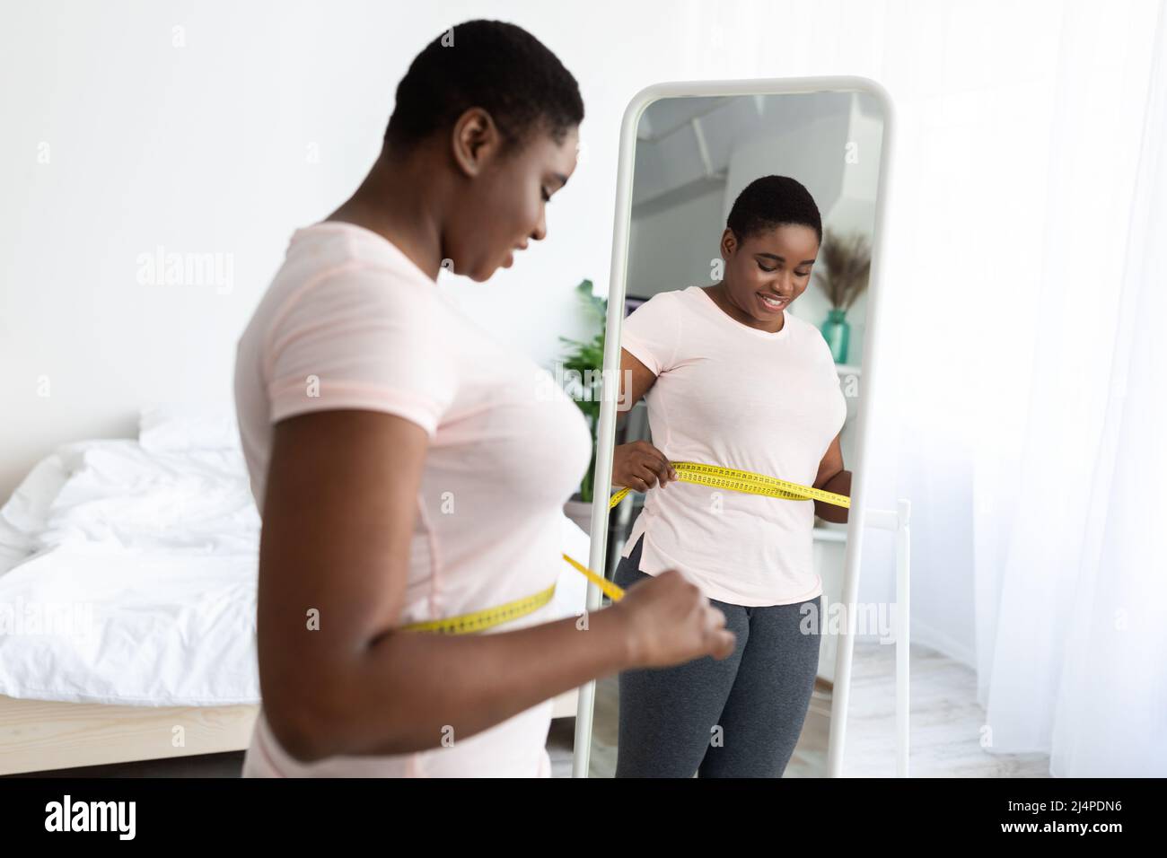 Taille plus noire femme mesurant la taille avec du ruban, debout près du  miroir, satisfait des résultats de l'alimentation amincissante à la maison  Photo Stock - Alamy