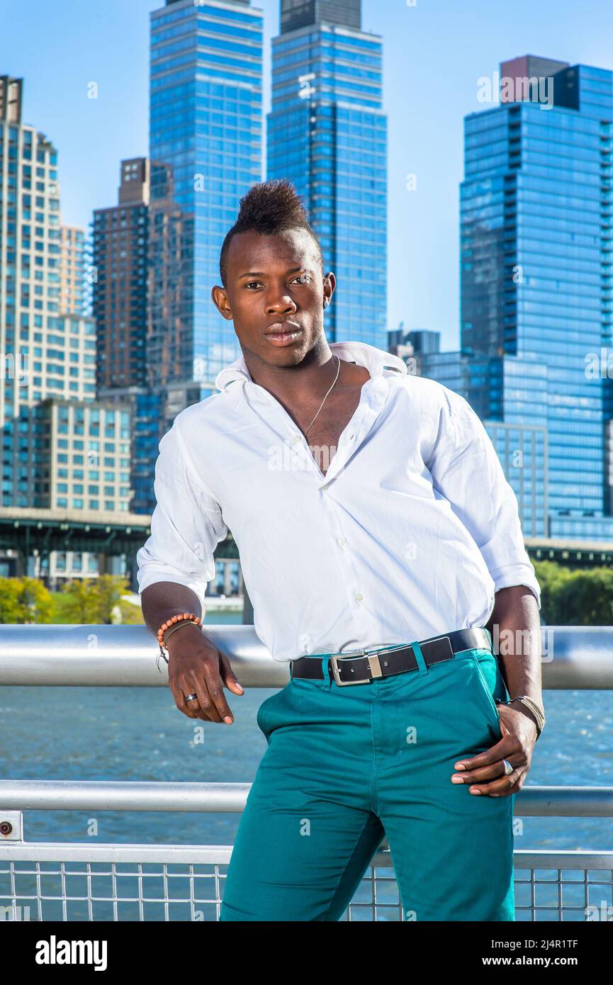 Portant une chemise blanche et un pantalon vert, un jeune homme noir avec  une coupe de cheveux mohawk se tient devant des hauts bâtiments modernes et  vous regarde Photo Stock - Alamy