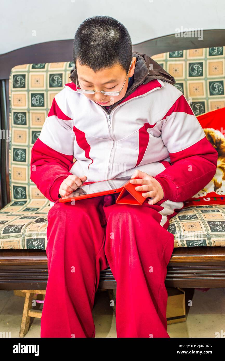 Jeune garçon lisant à la maison. Vêtues d'un uniforme scolaire, un adolescent regarde vers le bas une tablette. Banque D'Images