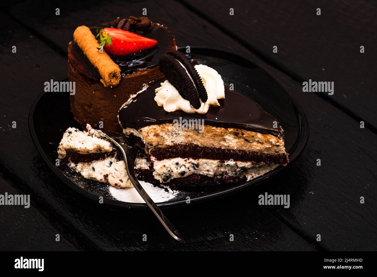 Mousse au chocolat chocolat, fraise stick et crémeux au chocolat cheesecake cookies, biscuits à la crème sur une assiette noire. Banque D'Images