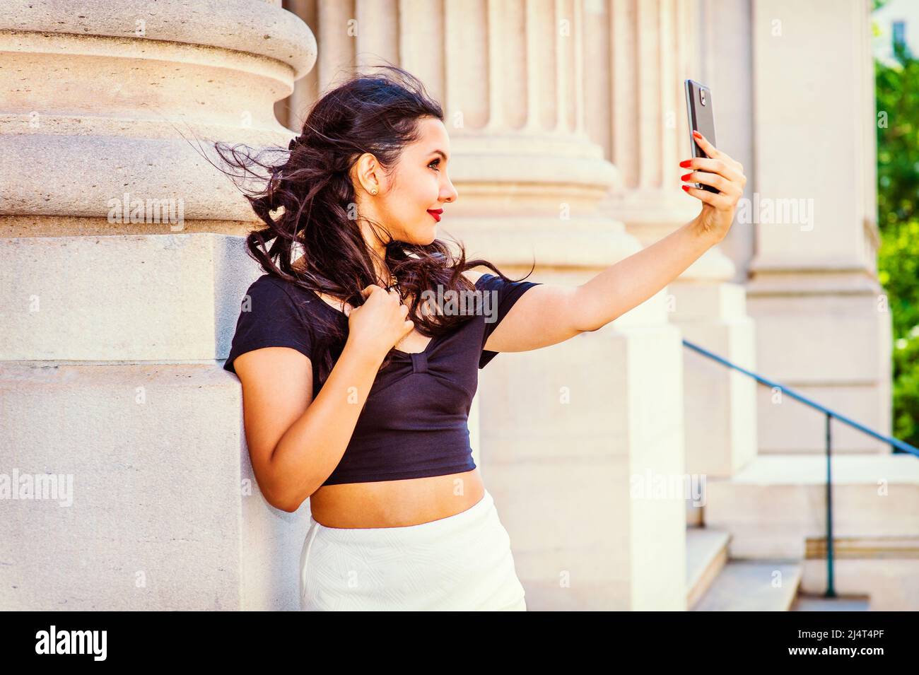 Belle fille a pris des photos de son soi. Bras étirant, tenant un appareil mobile, un jeune étudiant d'université regarde à travers une caméra à l'extérieur Banque D'Images