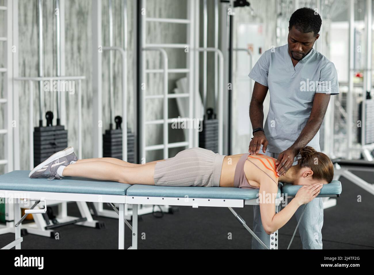 Thérapeute en réadaptation mettant du ruban kinésio sur le dos et l'épaule de la patiente dans la clinique de physiothérapie, l'espace de copie Banque D'Images