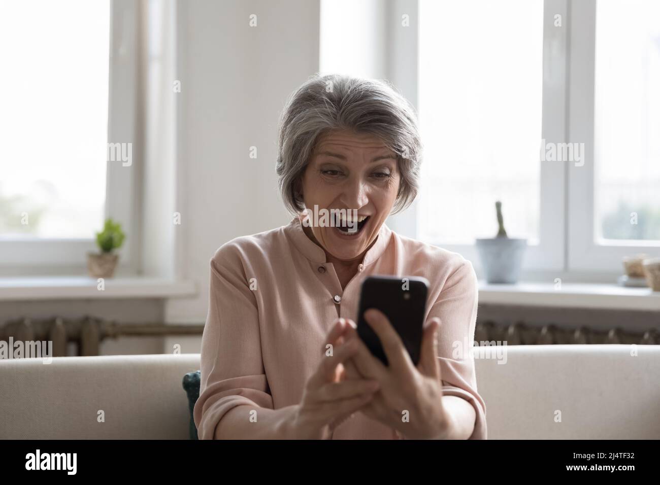 Femme plus âgée regardant à l'écran de téléphone cellulaire avec la bouche ouverte Banque D'Images