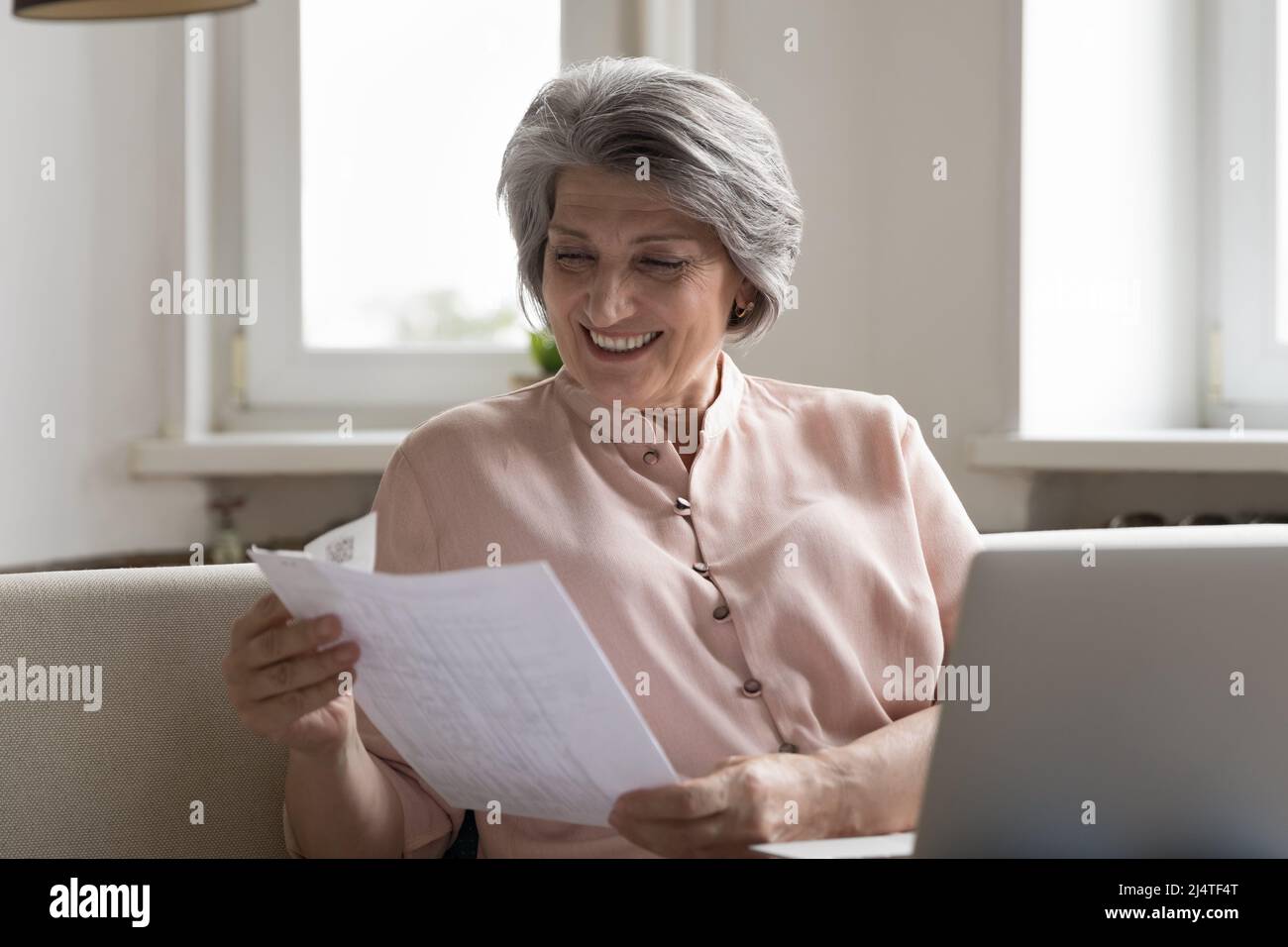 Une femme plus âgée souriante apprécie les bonnes nouvelles dans le document papier de lettre Banque D'Images