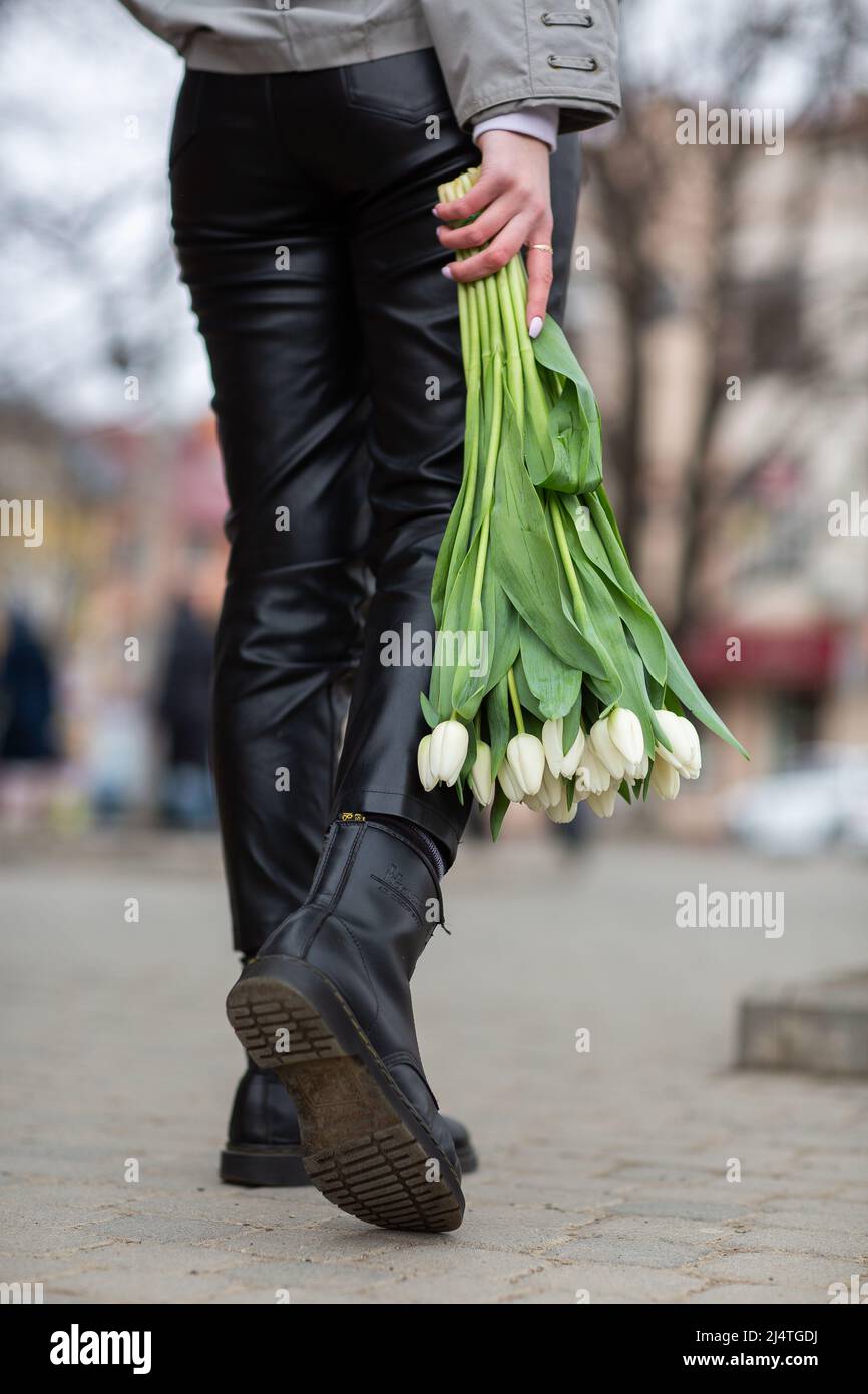 bouquet de tulipes blanches dans la main d'une fille . fille tenant des fleurs sur le fond de belles jambes. concept de printemps, couleurs de printemps fraîches Banque D'Images