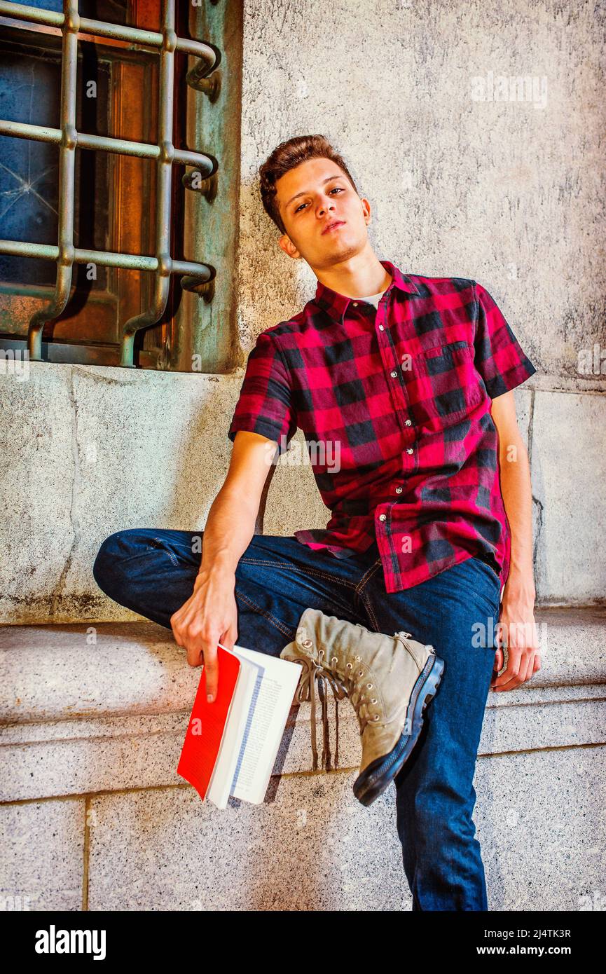 Homme relaxant dehors. Robe de chambre à manches courtes, chemise noire, rouge à motifs, jeans, chaussures de marche, un jeune homme beau est assis près d'une fenêtre, tête lea Banque D'Images