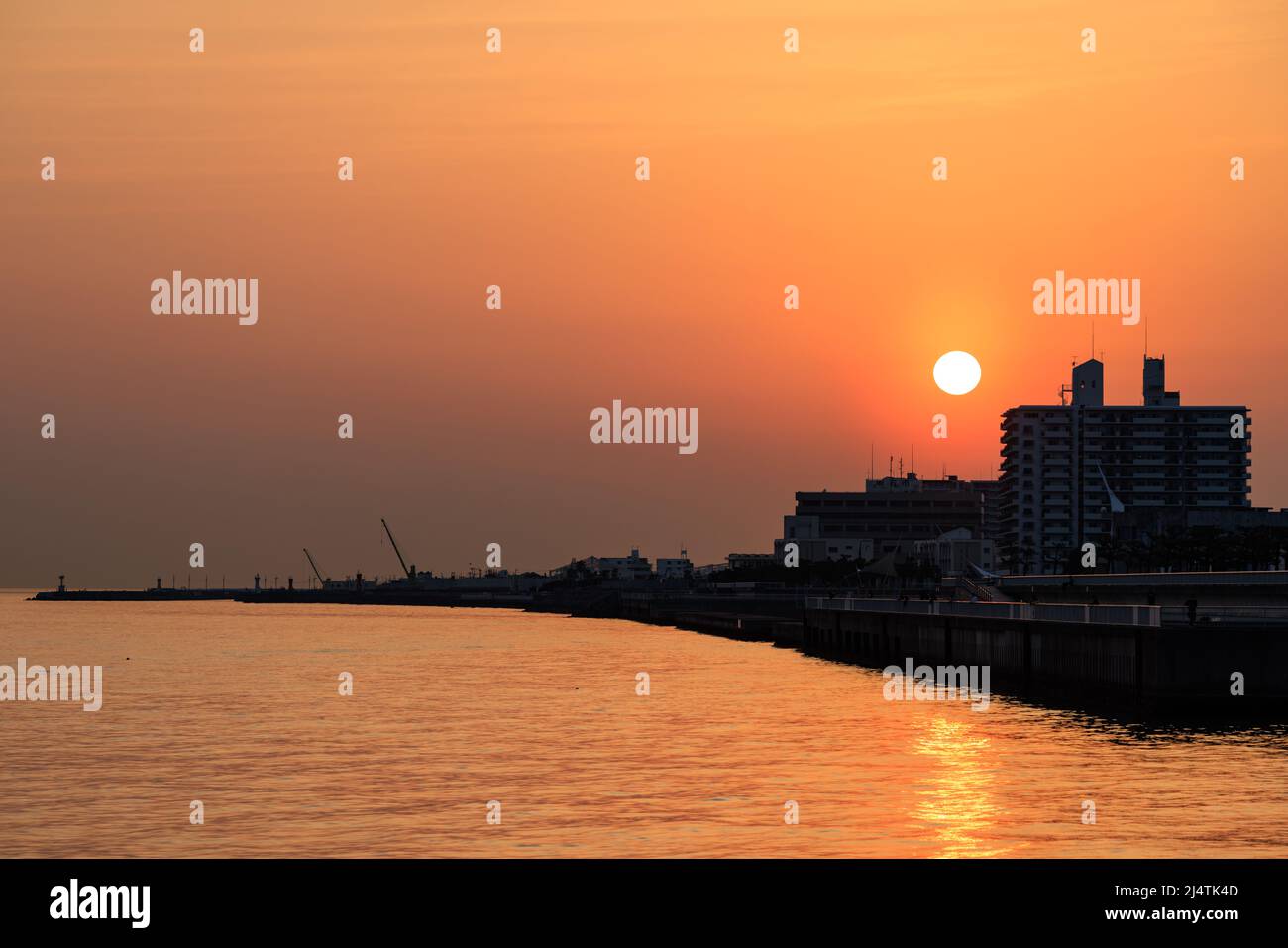 Le soleil se couche à travers la brume orange sur les bâtiments silhouettés sur la côte Banque D'Images