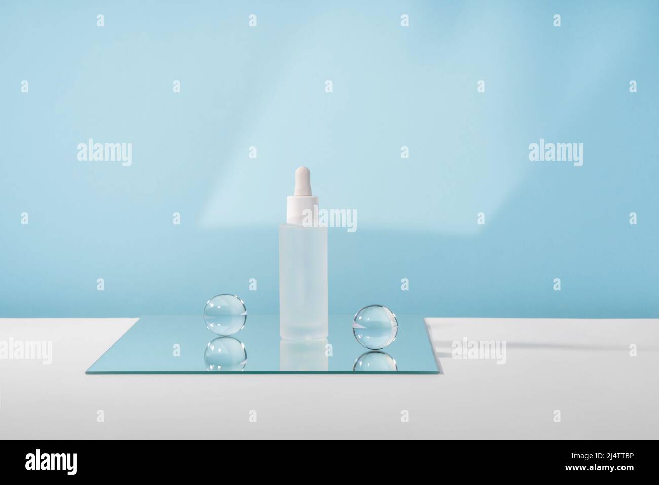 Flacon cosmétique de sérum avec peptides et rétinol sur miroir avec billes de verre sur fond bleu. Emballage de maquette de produit cosmétique à l'acide hyaluronique Banque D'Images