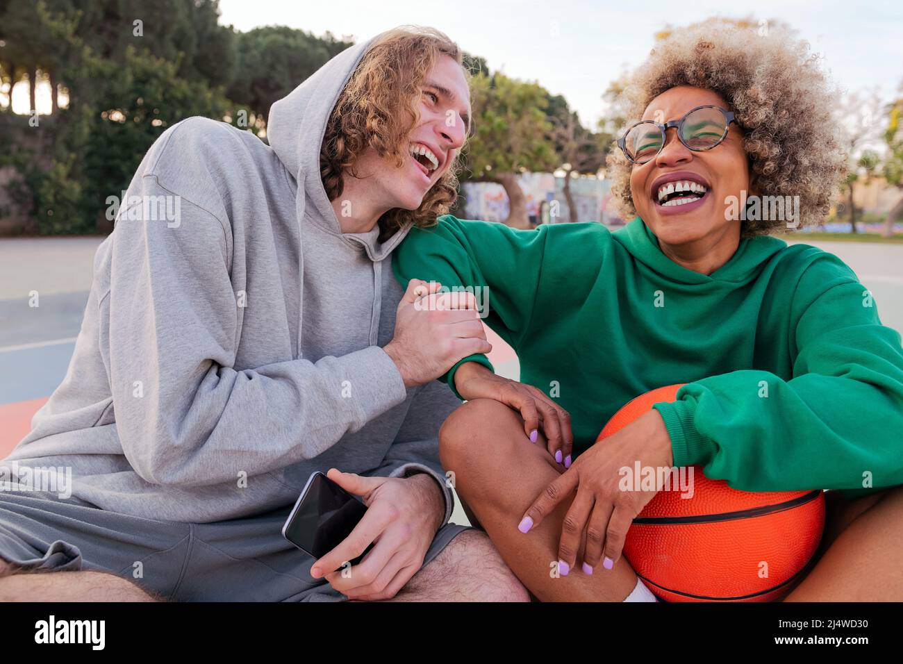 amis riant en partageant un bon moment assis après avoir joué au basket-ball dans un parc de ville, concept d'amitié et de sport urbain dans la rue Banque D'Images