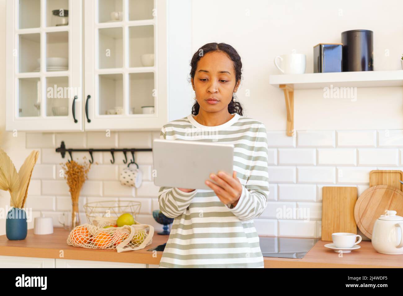 Femme afro-américaine à la recherche d'une recette sur un PC tablette avant de cuisiner un repas dans la cuisine Banque D'Images