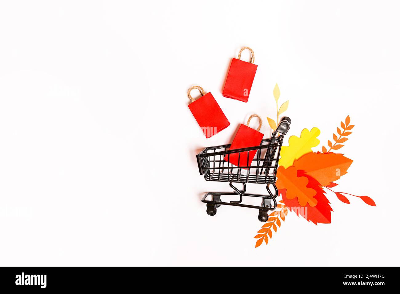 chariot d'épicerie d'automne avec sacs en papier et feuilles rouges tombant sur fond blanc. Concept vente d'automne. Espace de copie Banque D'Images