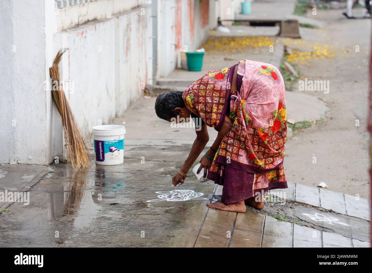 Femme dessinant un Kolam (muggulu) - forme de peinture dessinée en utilisant de la poudre de riz sur le trottoir devant la maison, Trichy, Tamil Nadu, Inde Banque D'Images
