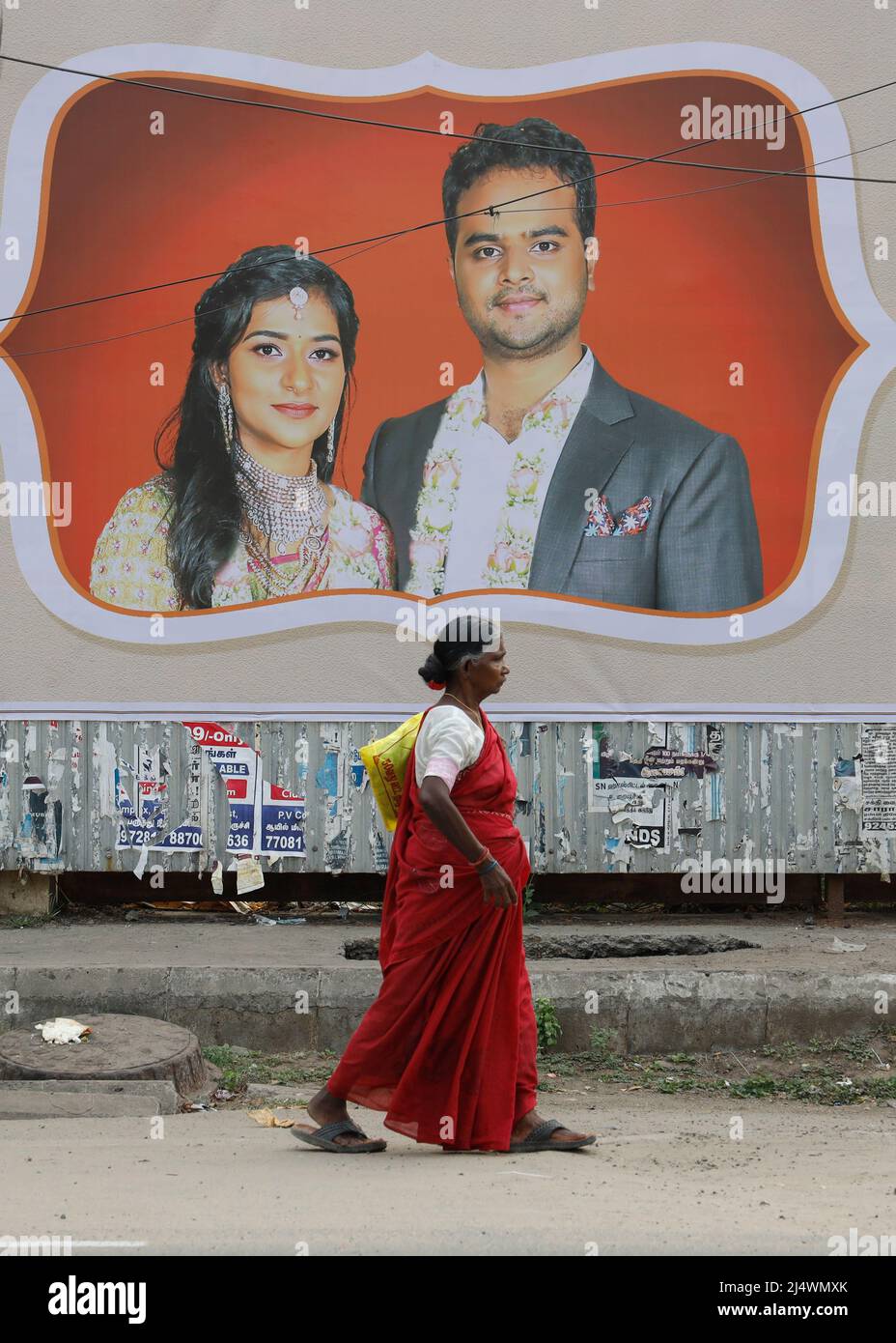 Une vieille femme marchant devant un mur couvert par un poster de campagne électorale à Trichy, Tamil Nadu, Inde Banque D'Images