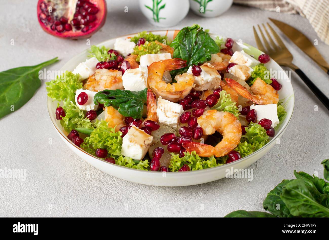 Salade de crevettes, ananas, feta et graines de grenade dans une assiette sur des feuilles de laitue vertes, sur fond gris Banque D'Images