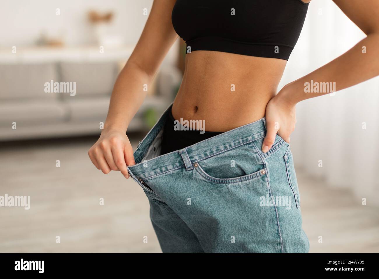 Une dame noire non reconnaissable montrant des muscles abdominaux portant des jeans surdimensionnés en intérieur Banque D'Images