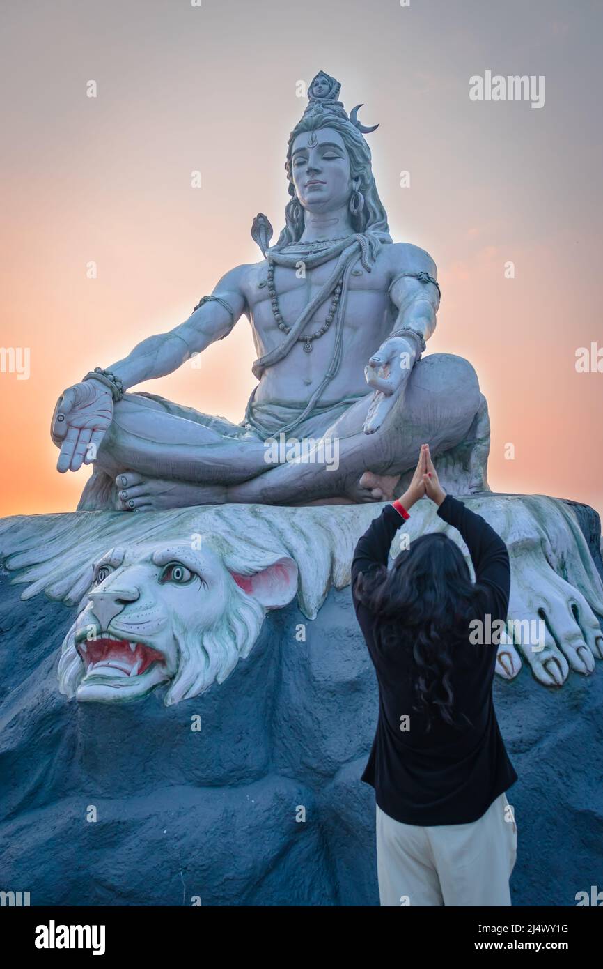 une fille priant à la statue de dieu hindou de shiva en posture de méditation avec ciel dramatique à l'image du soir est prise à parmarth niketan rishikesh uttrakhhand Banque D'Images