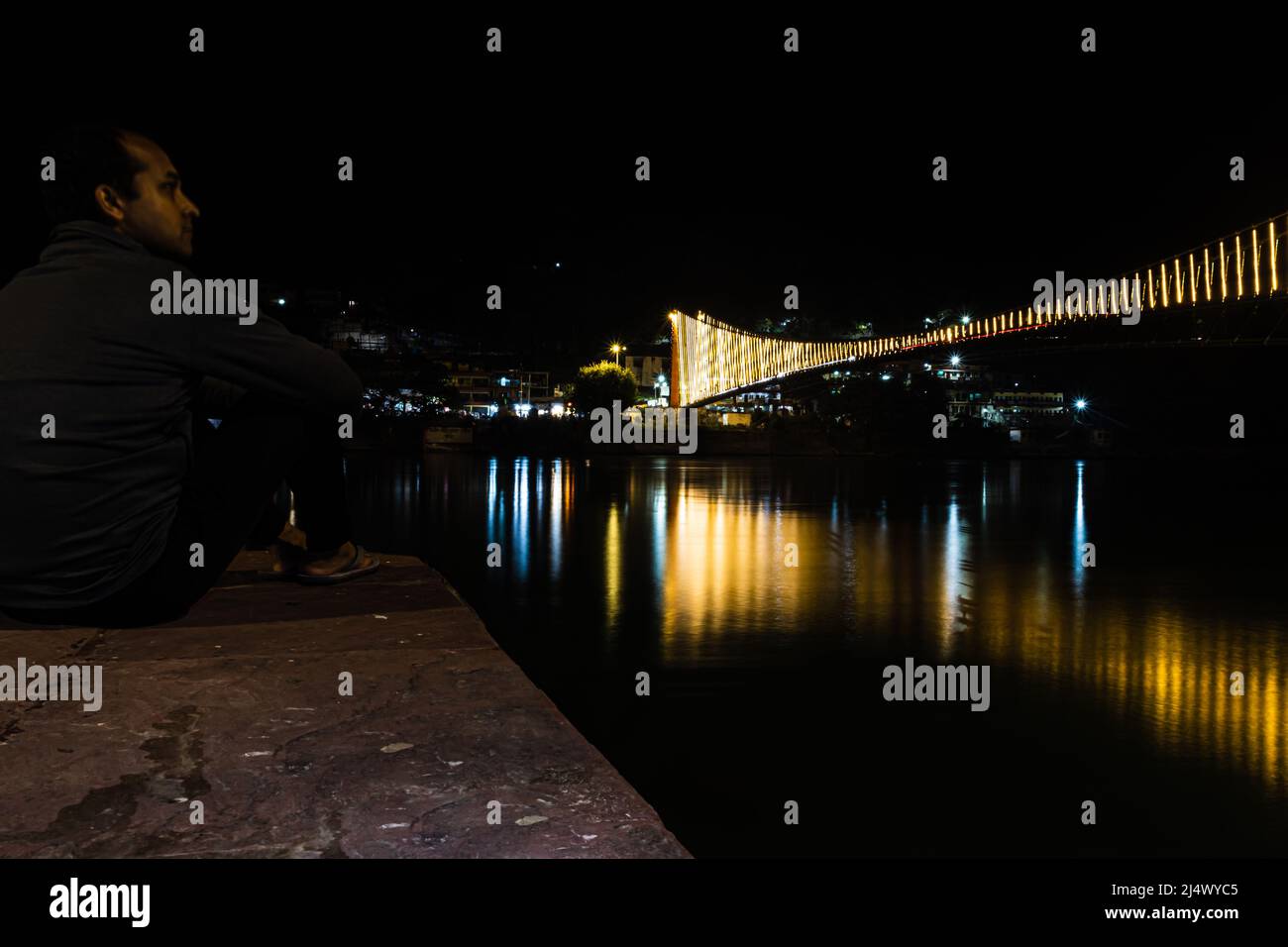 homme regardant le pont de suspension de fer illuminé avec des lumières de ferry avec l'image de réflexion d'eau est prise à rishikesh uttrakhet inde. Banque D'Images