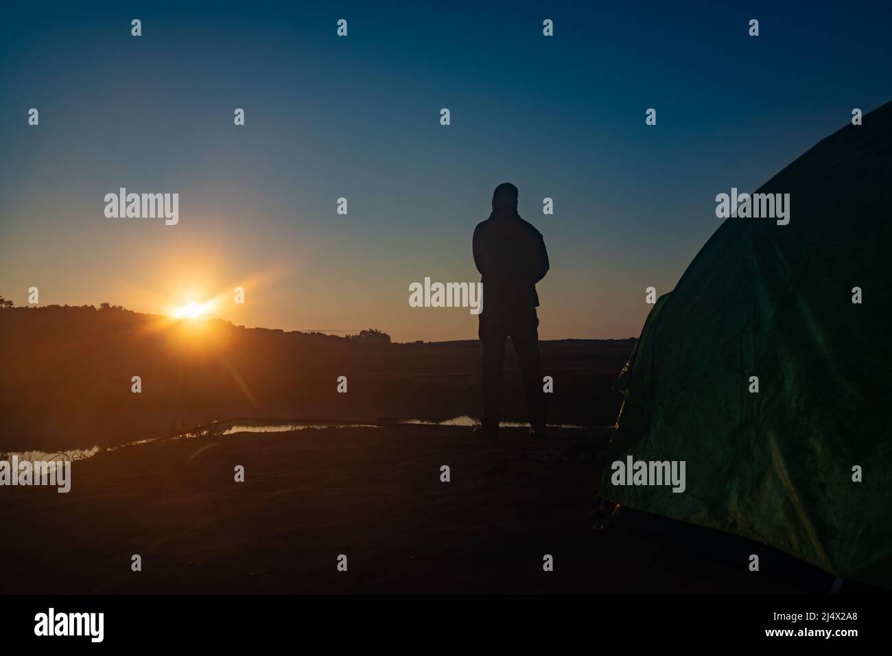 homme rétroéclairé debout au lever du soleil sur l'ombre de la montagne et lac calme avec réflexion le matin Banque D'Images