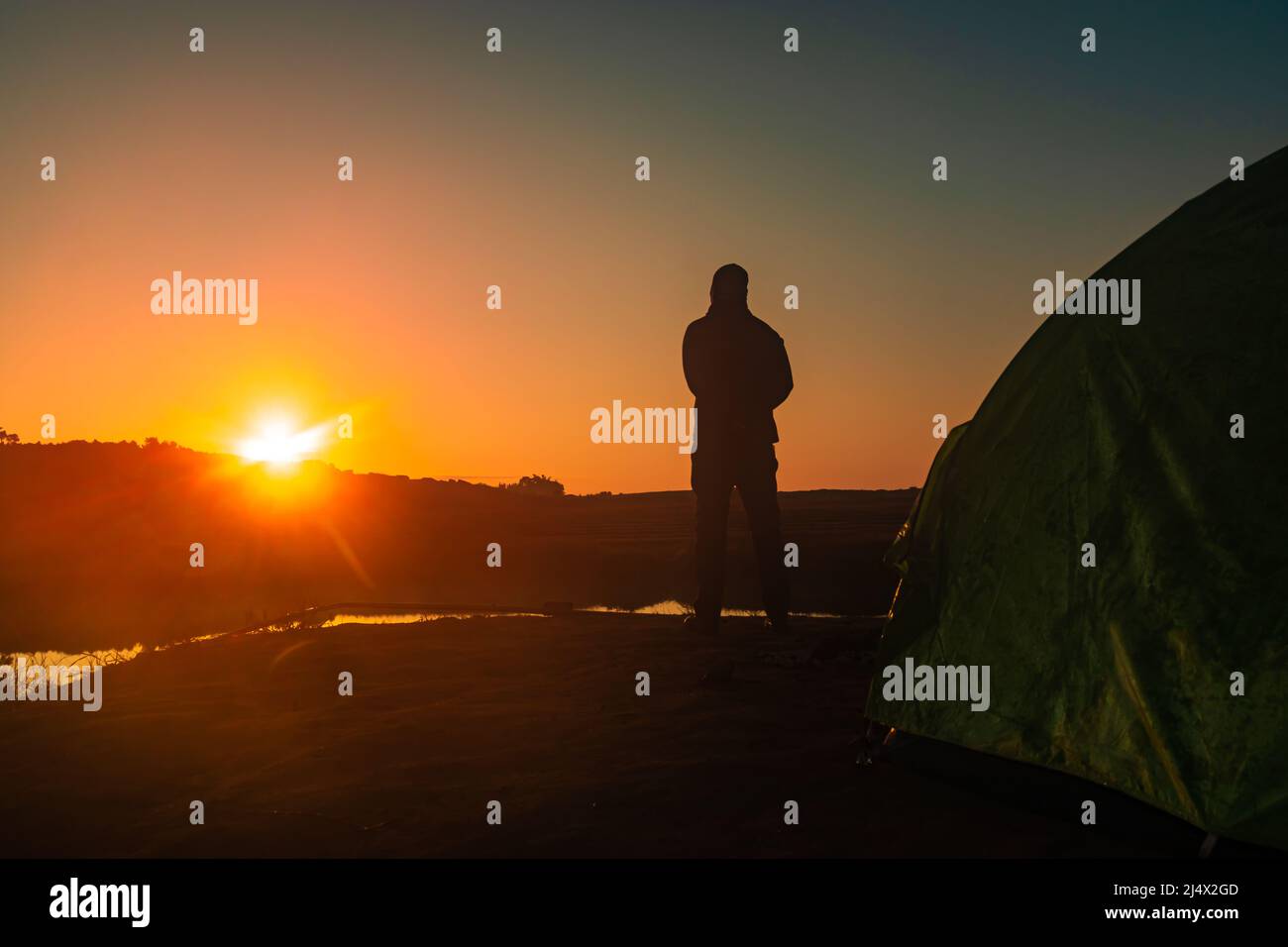 homme rétroéclairé debout au lever du soleil sur l'ombre de la montagne et lac calme avec réflexion le matin Banque D'Images
