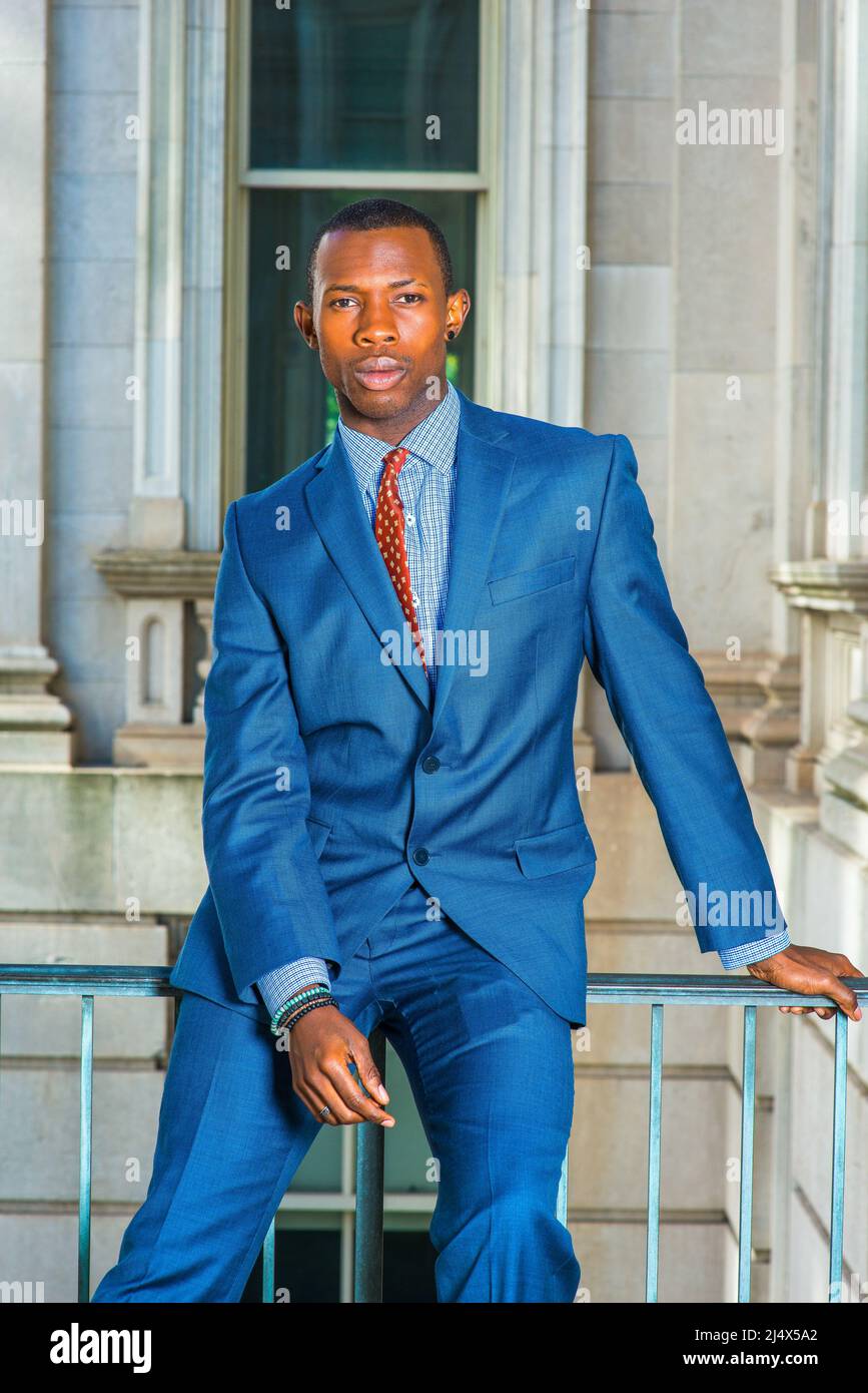 Homme d'affaires qui pense dehors. Dressing formellement en costume bleu,  cravate à motifs, un jeune homme noir assis sur une rampe dans un immeuble  de bureau de style vintage, moi Photo Stock -