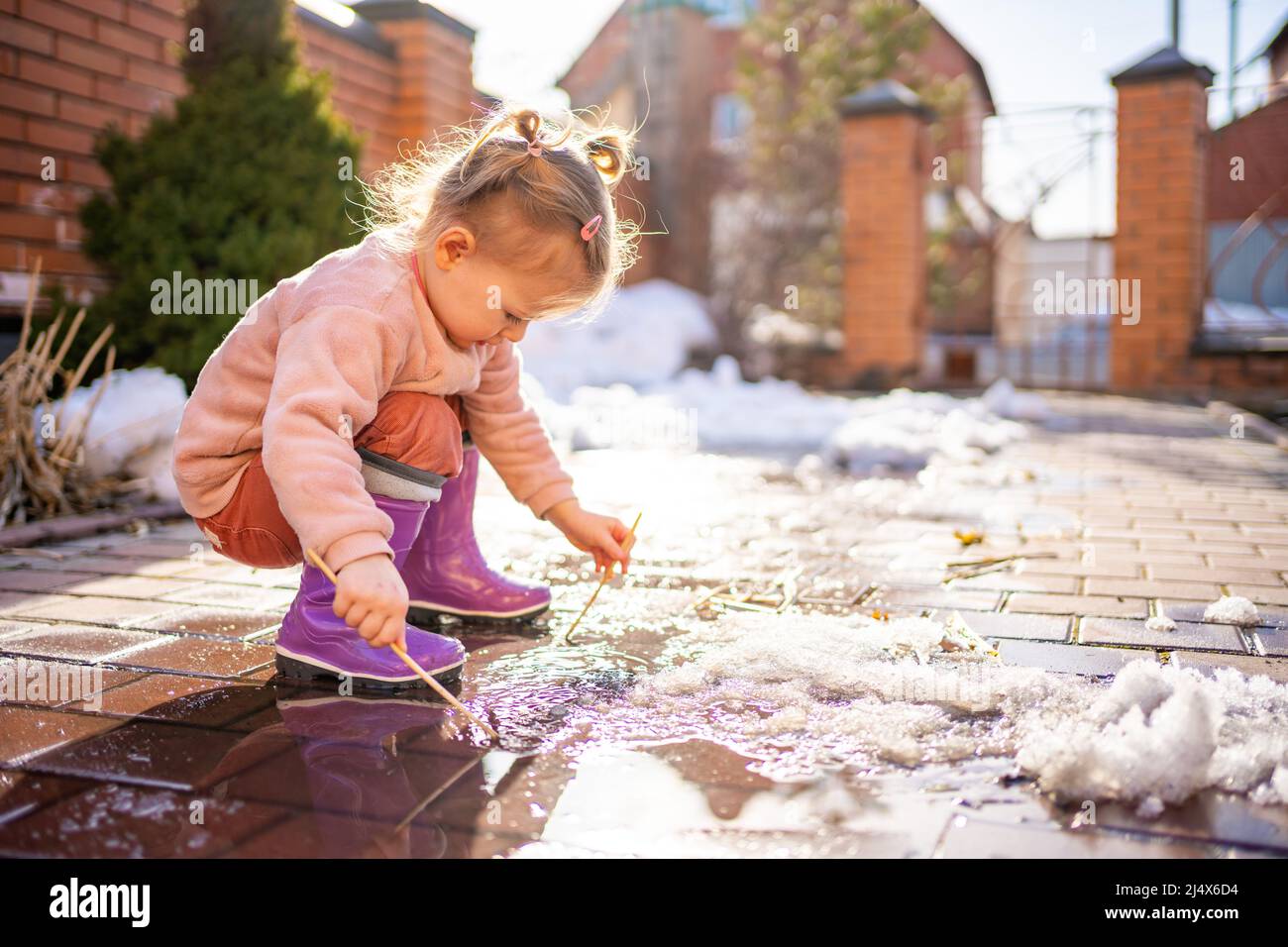 Fille joue dans une flaque avec bâton de bois dans le jour de printemps à la lumière du soleil Banque D'Images