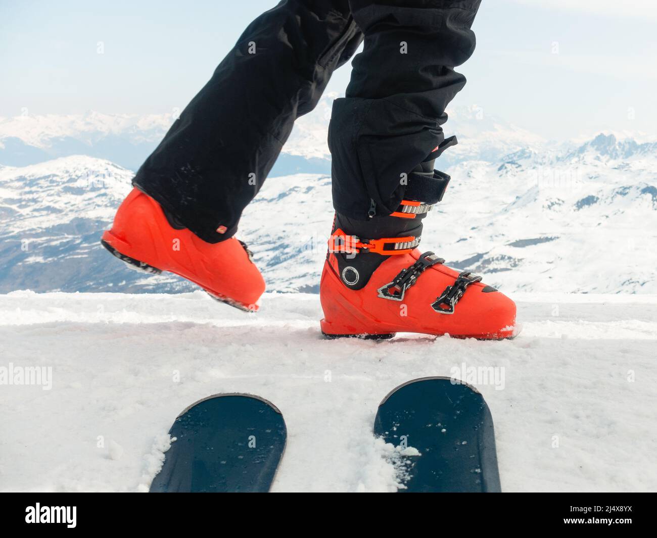 Skieur en bottes de ski rouges marchant sur le bord de la montagne avec le sommet ovale des skis et la grande crête de montagne à distance Banque D'Images