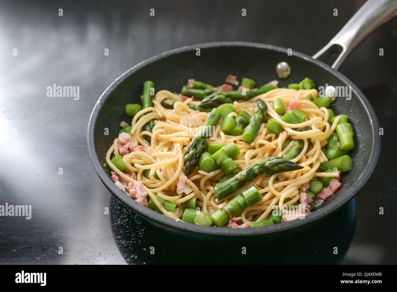 Spaghetti aux asperges vertes et bacon dans une casserole noire sur la cuisinière, cuisson d'un délicieux plat de pâtes, espace de copie, foyer sélectionné, profondeur étroite de fiel Banque D'Images