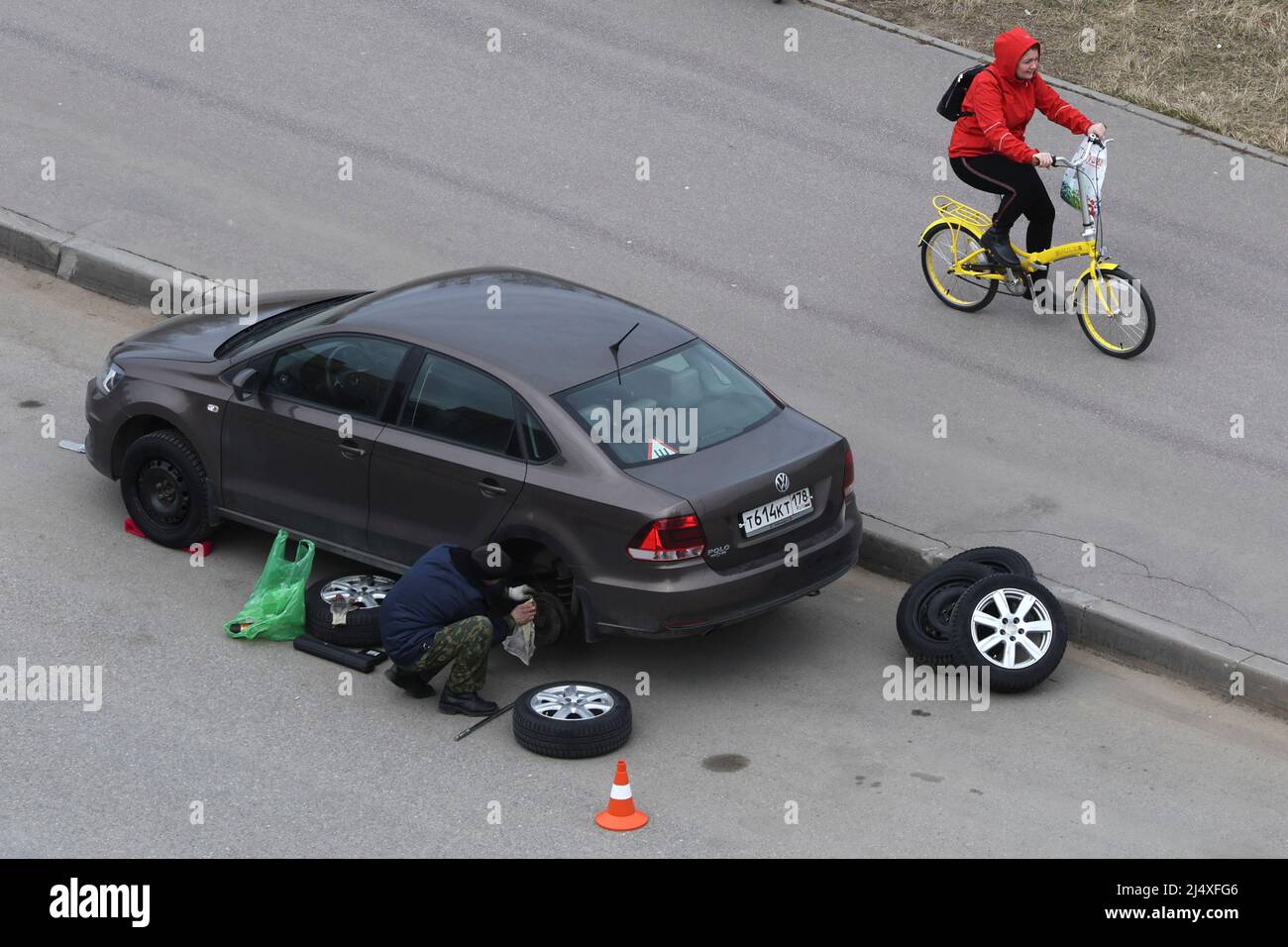 Un conducteur change de roue sur une voiture alors qu'un cycliste passe à la périphérie de Saint-Pétersbourg, Russie le 18 avril 2022. PHOTOGRAPHE REUTERS/REUTERS Banque D'Images