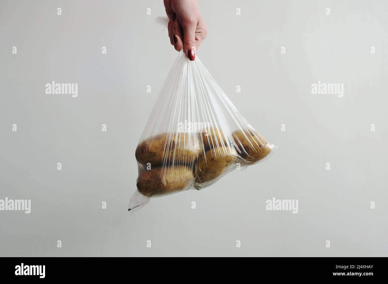 La main de la femme tient les pommes de terre dans un sac en plastique. Aliments emballés dans un emballage cellophane sur fond gris. Emballage non écologique Banque D'Images