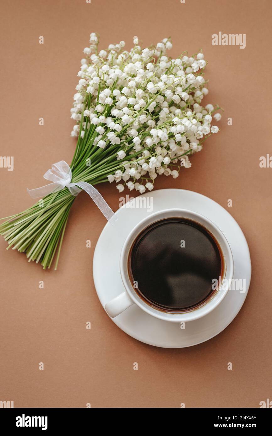 Tasse à café avec bouquet de fleurs lis de la vallée sur fond beige vue de dessus. Pose à plat. Banque D'Images
