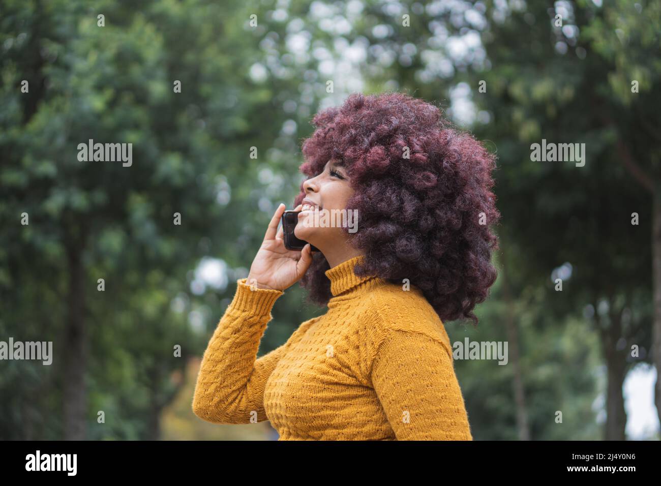 Une jeune femme afro est en communication téléphonique avec son téléphone cellulaire à l'extérieur. Banque D'Images