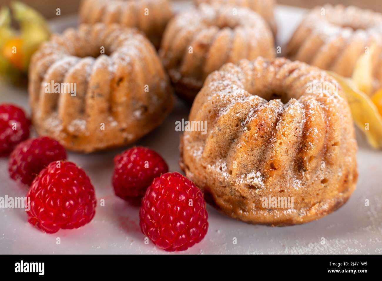 Délicieux gâteaux sucrés sur une assiette blanche avec du sucre sur le dessus, des framboises et des baies dorées en dessous. Bonbons faits maison pour en-cas ou petit-déjeuner. Nourriture. Banque D'Images