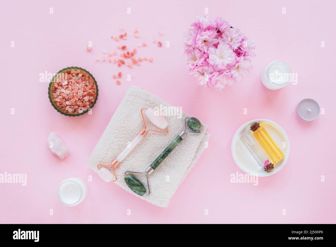 Ensemble de cosmétiques naturels bio spa avec fleurs de sakura. Plat déposer le sel de bain, les rouleaux de visage, les fleurs de cerise, la crème cosmétique et l'huile sur fond rose. Banque D'Images