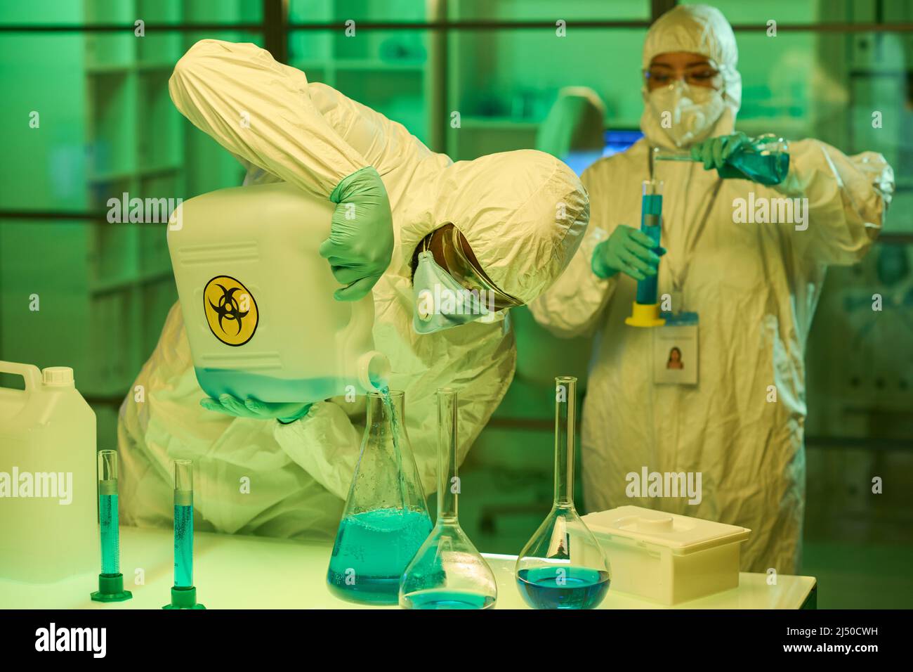 Employé contemporain de laboratoire clinique mélangeant des substances liquides dans des tubes à essai tout en se pliant sur le lieu de travail contre une collègue féminine Banque D'Images