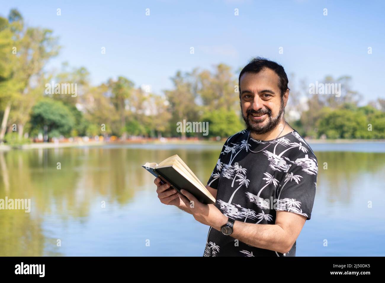 Homme mature lisant au bord d'un lac, profitant de temps libre par une journée ensoleillée Banque D'Images
