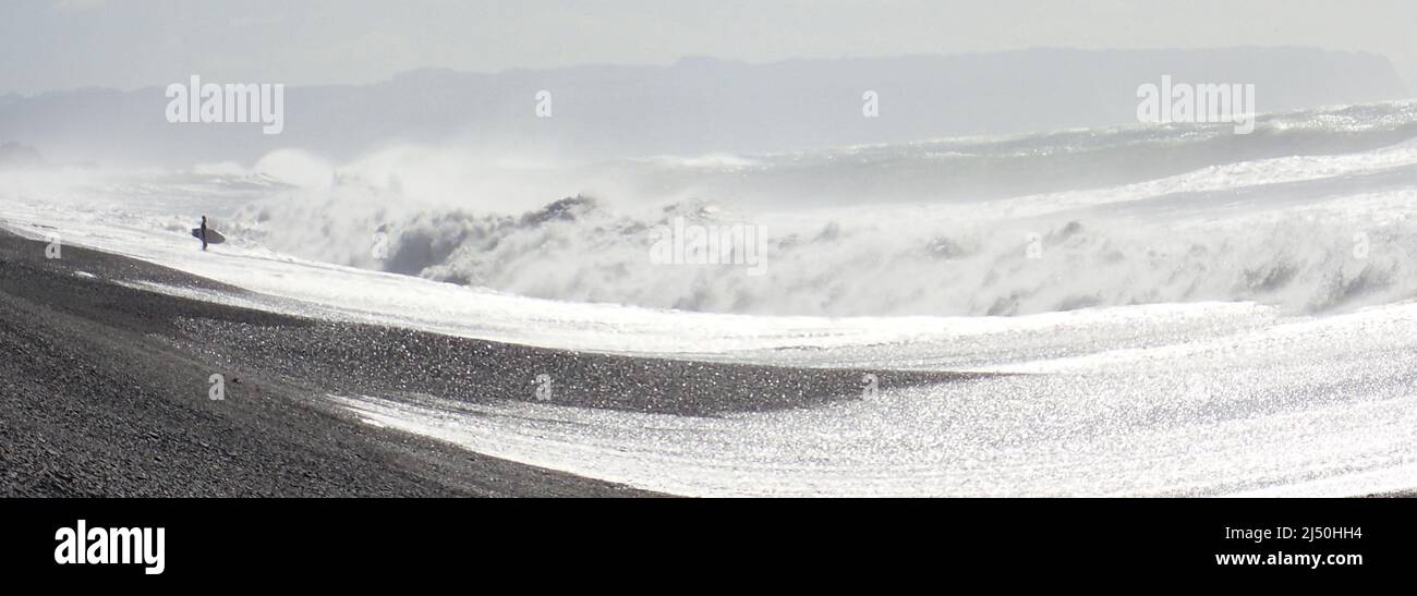 Un surfeur solitaire qui attend le bon moment pour entrer, avec des vagues sauvages s'écrasant sur la Marine Parade Napier Banque D'Images