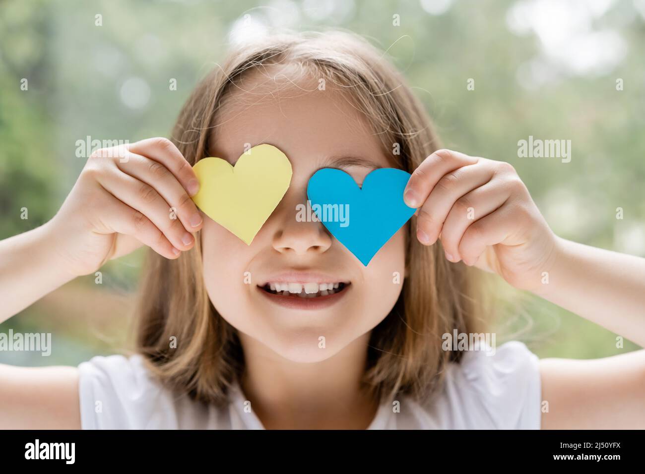 joyeuse fille ukrainienne obscurcissant le visage avec des coeurs en papier bleu et jaune Banque D'Images