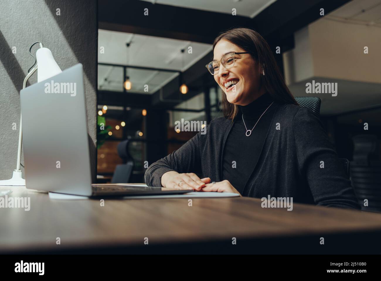 Femme d'affaires souriante assistant à une réunion en ligne dans un bureau de travail commun moderne. Une femme entrepreneure heureuse qui communique avec ses associés commerciaux Banque D'Images