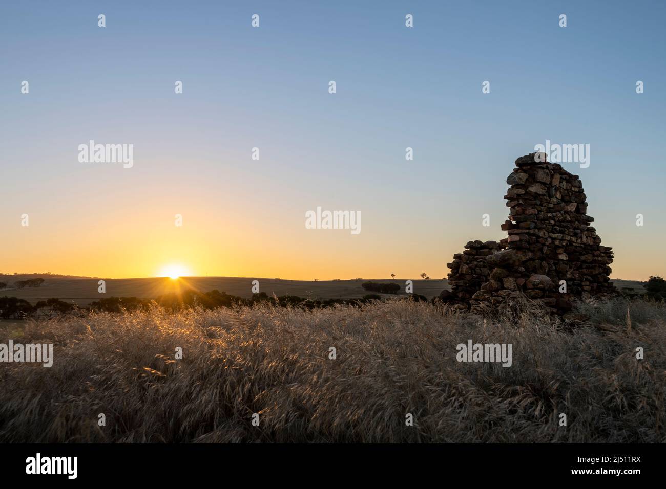 Coucher de soleil dans la ceinture de blé de l'Australie occidentale avec ruines de pierre ancienne en premier plan. Banque D'Images