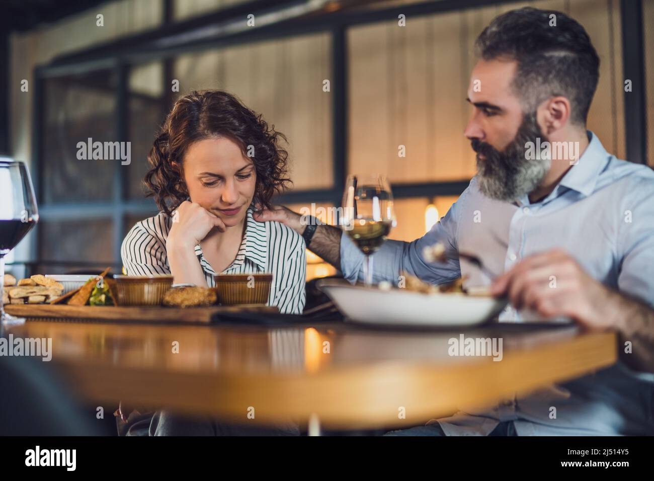 Un couple adulte est assis au restaurant. Ils dînent avec du vin. La femme est triste et déprimée. Banque D'Images