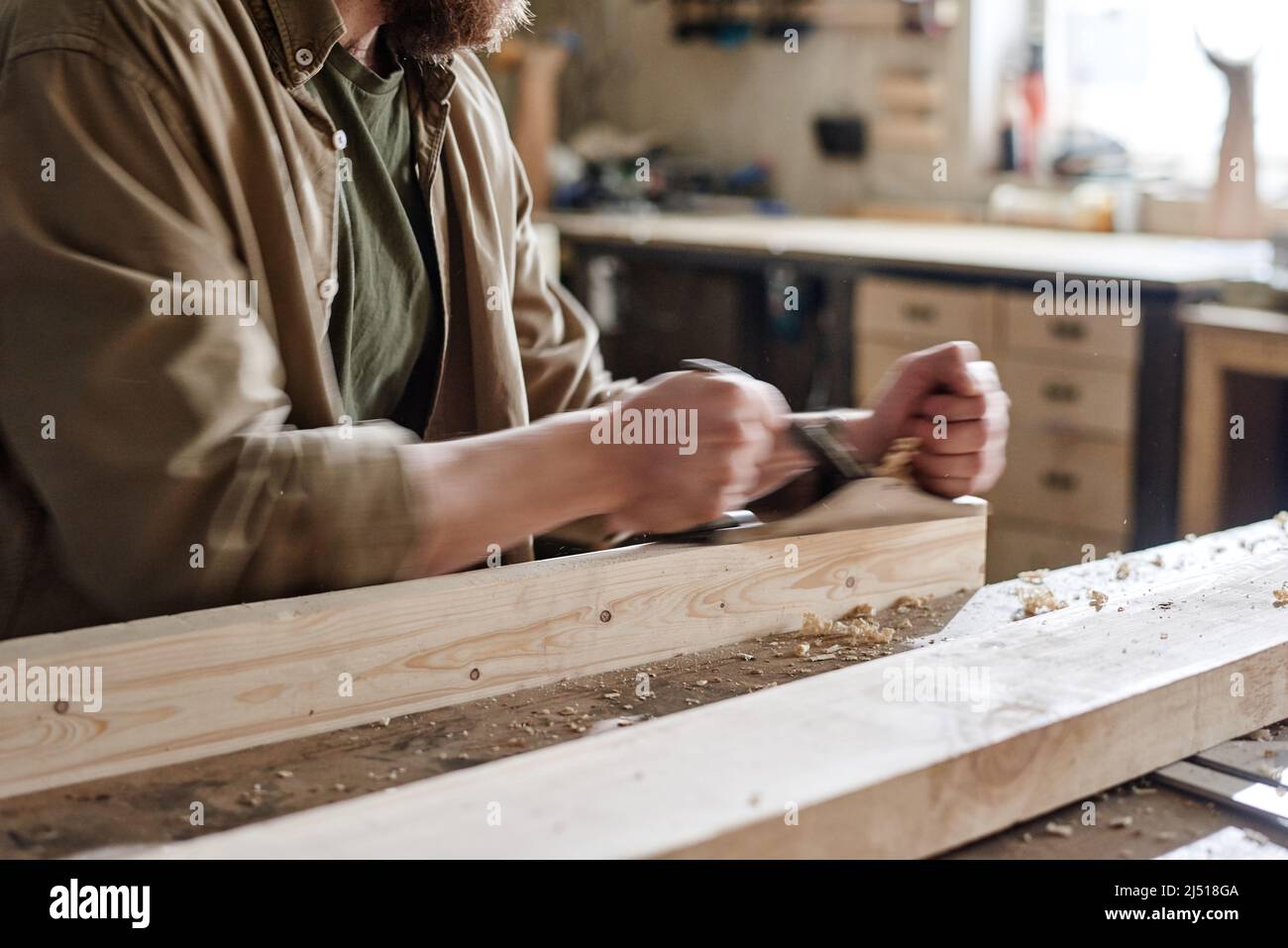 Menuisier mâle professionnel travaillant dans l'atelier à l'aide d'un rabot à main pour lisser la surface de la planche en bois Banque D'Images