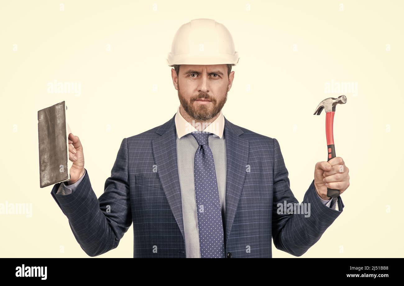 L'ingénieur du bâtiment porte un casque de sécurité avec une combinaison classique, un marteau et une truelle, une finition en plâtre Banque D'Images